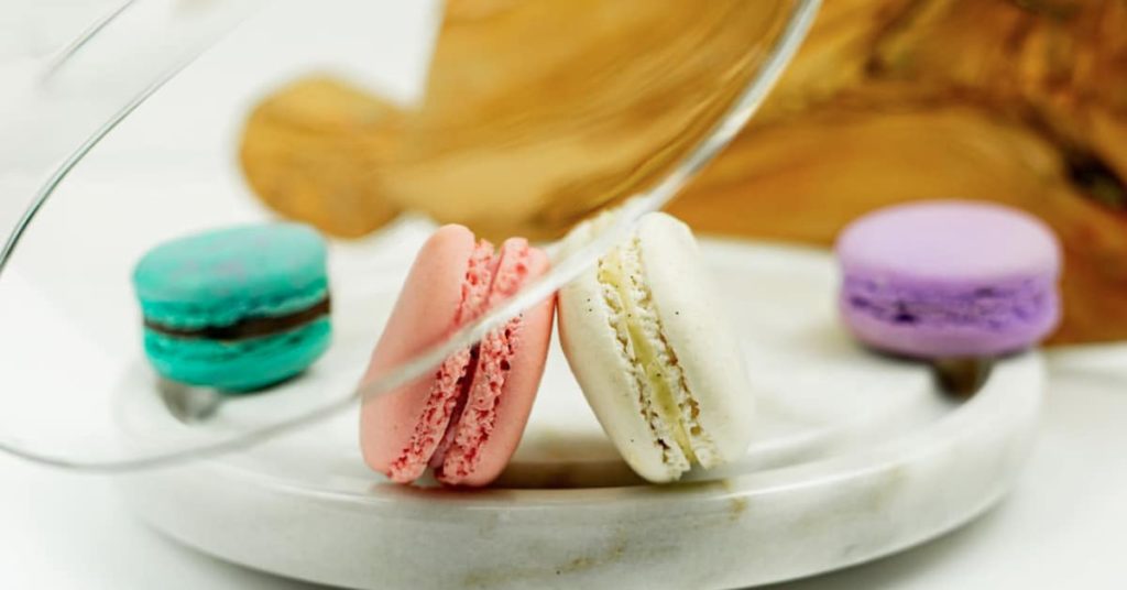 say please in french to these macarons of different colours on a plate.